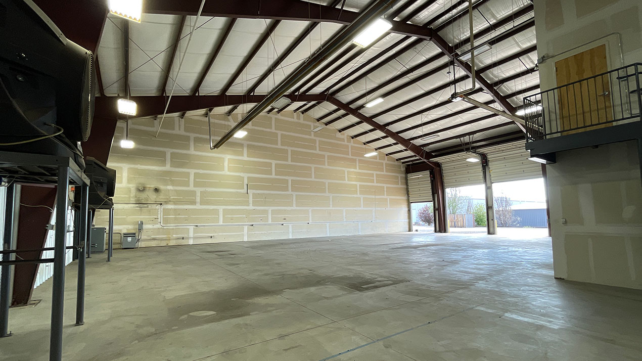 Large empty warehouse with high ceiling, concrete floor, and open bay doors at the far end.